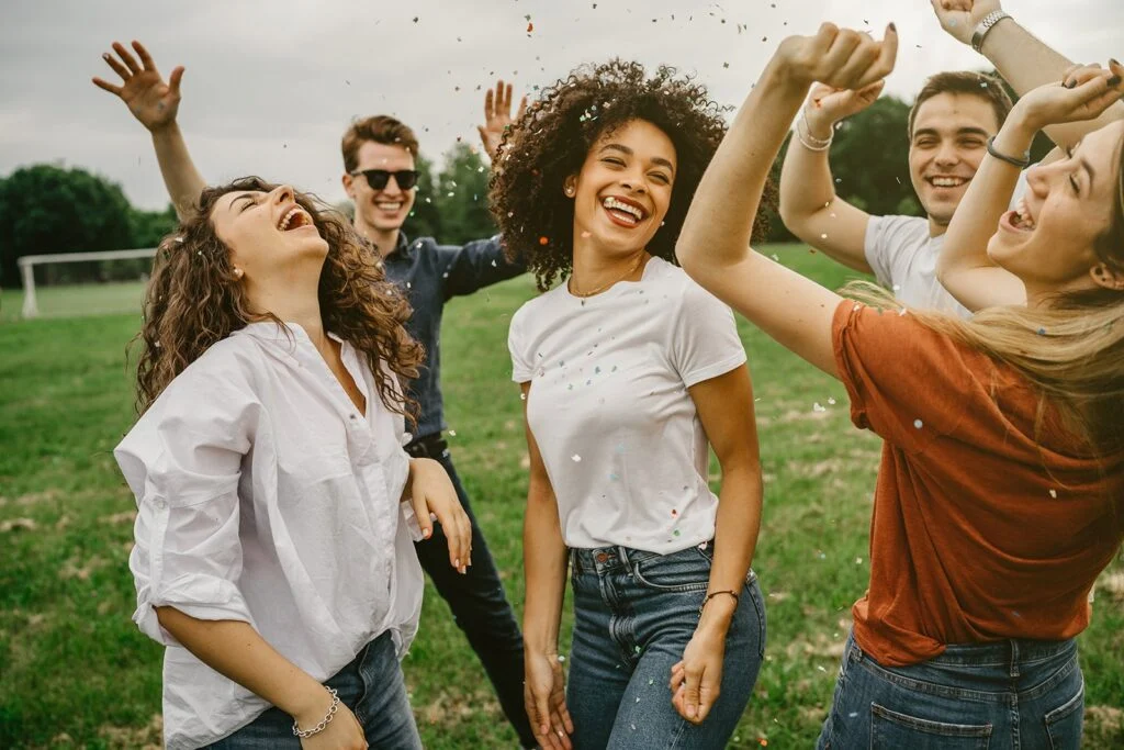 Young friends laughing and dancing together on a lawn