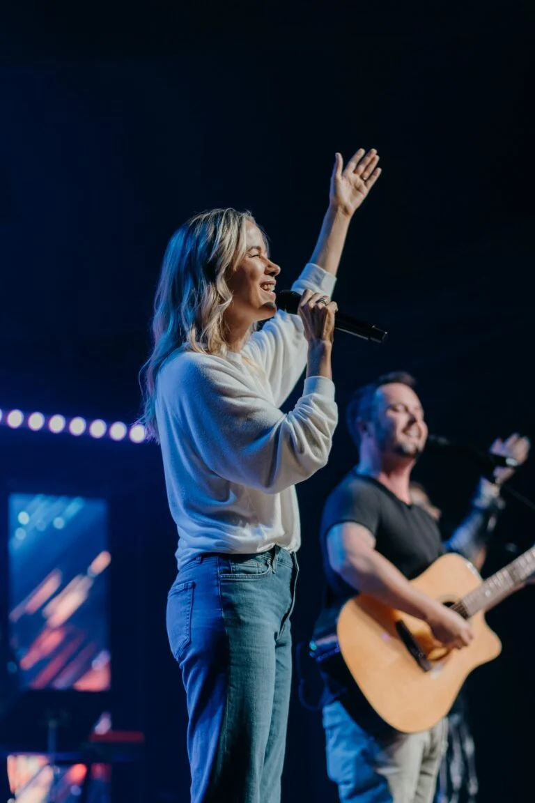 A woman singing and a guitarist playing on a blue-lit stage
