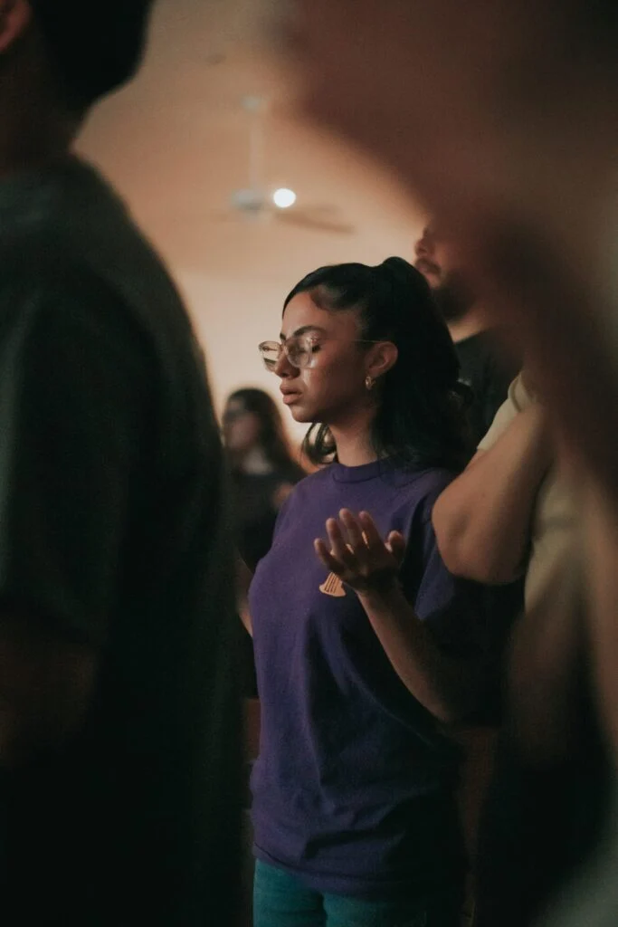 A young woman in a purple shirt praying with her hands together