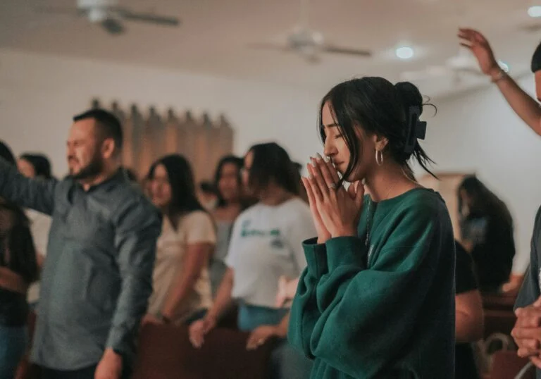 A woman praying with hands together among a standing congregation