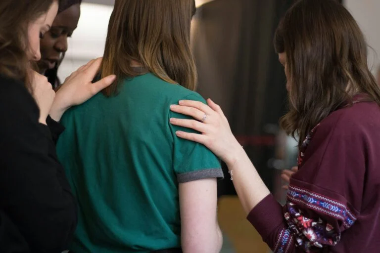 Friends with their hands on each other shoulders in prayer